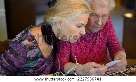 Extreme closeup of elderly woman looks at photos with daughter. Senior woman sitting in the dining room looking at photographs with daughter. Brain training. Memory activity.