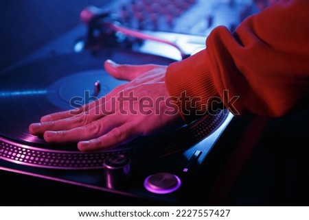 Hip hop DJ scratching records on turntables. Club disk jokey scratches vinyl disc on turn table in night club Royalty-Free Stock Photo #2227557427