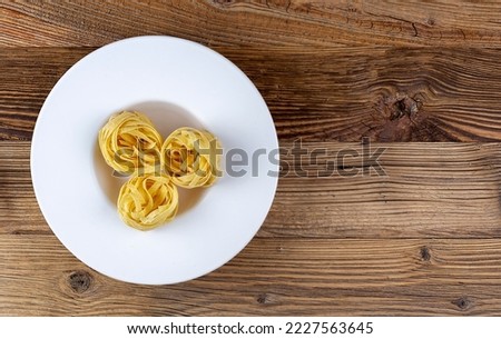 Raw pasta in white plate on a wooden background, top view, copy space
