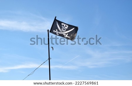 Pirate flag with skull and swords on blue sky background.
