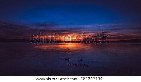 A panoramic view of the afterlife on a beautiful sunset with strong colors on a mirror-smooth lake in midsummer. Beautiful sight. Royalty-Free Stock Photo #2227591391