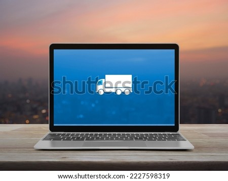 Delivery truck flat icon on modern laptop computer screen on wooden table over blur of cityscape on warm light sundown, Business transportation online service concept