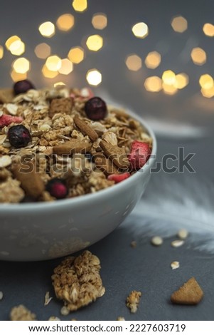 A bowl of muesli on a gray monochrome background, with white feathers and a side from a garland. Healthy food, healthy breakfast