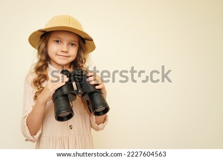 Traveler child. Child discoverer. Young researcher. Little girl in a safari hat with binoculars in her hands. Concept: search for adventure and treasure. Cute happy girl in safari clothes Royalty-Free Stock Photo #2227604563