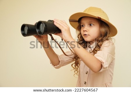 Traveler child. Child discoverer. Young researcher. Little girl in a safari hat with binoculars in her hands. Concept: search for adventure and treasure. Cute happy girl in safari clothes Royalty-Free Stock Photo #2227604567