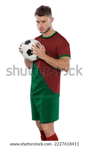 Professional soccer player in Portugal national team red and green jersey with ball in hands staring with challenging expression on white background.