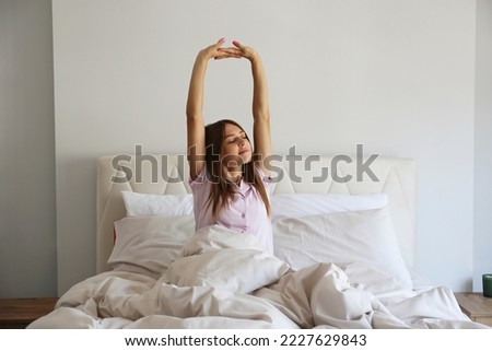 Young beautiful woman stretching in her bed after waking up in the morning. Sleepy brunette female with satisfied facial expression. Healthy sleeping habits concept. Close up, copy space, background. Royalty-Free Stock Photo #2227629843