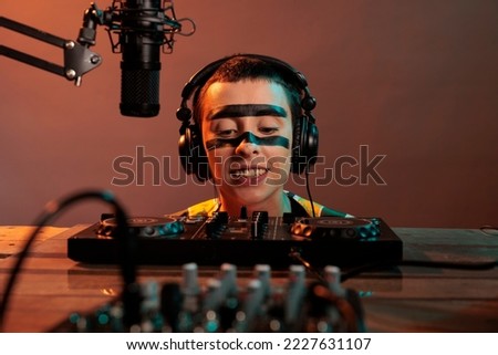 Musical artist acting funky looking at mixer, being focused on control buttons at dj turntables over background. Looking closely at audio equipment to mix techno music, stereo instrument.
