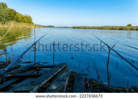 Fishing rods, a rotating reel on the river bank. Sunrise. Fog on the background of the lake. Foggy morning. Wildlife. The concept of rural recreation. Article about fishing day.
