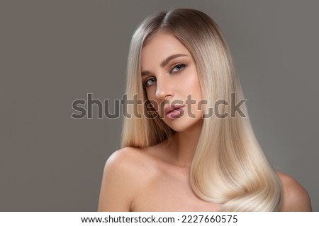 Beautiful young blonde with straight shiny hair. Portrait on a gray background. Hair and makeup Royalty-Free Stock Photo #2227660575