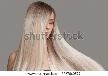 Beautiful young blonde with straight shiny hair. Portrait on a gray background. Hair and makeup Royalty-Free Stock Photo #2227660579