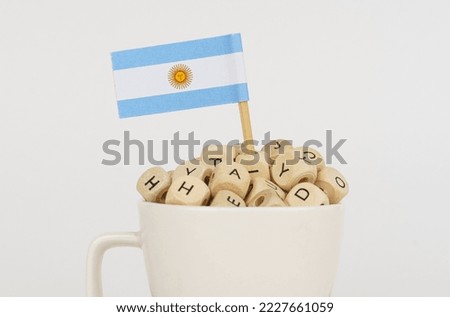 The flag of Argentina sticks out of a cup with dice on which letters are depicted. Symbol of education. close-up