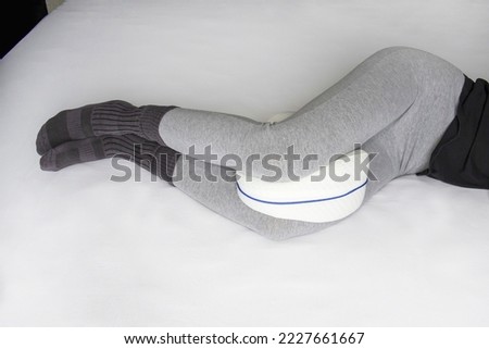 Young woman in pajama pants with an anatomical pillow between her legs and knees, lying on a bed with white sheets Royalty-Free Stock Photo #2227661667