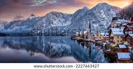 Panoramic view of the little village of Hallstatt, Austria, during winter sunset time with snow, glowing sky in the mountains and warm lights from the houses