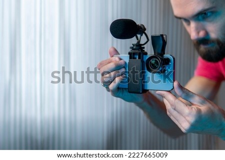 A young man sets up his phone to shoot a video. A lens and microphone are installed on the phone. Smartphone videography concept