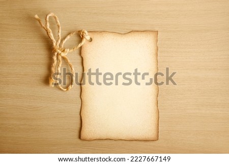 Paper label with old parchment texture, worn edges and a rope tied in the shape of a bow on a light brown wooden surface