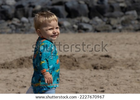 Young Toddler boy child at the beach in fasionable outfit turns and smiles towards the camera