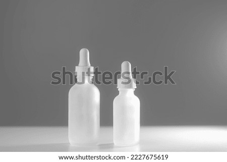 Two empty white translucent glass dropper vials beside each other on two-tone white backdrop. Different-sized bottles placed center. Horizontal beauty background, mockup, and copy space.