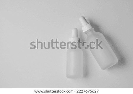 Two empty translucent glass dropper vials. Flatlay of different-sized bottles lying on white surface. Horizontal beauty and lifestyle background, mockup, and copy space. Professional lighting. Royalty-Free Stock Photo #2227675627