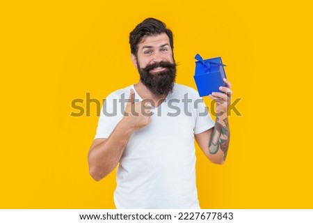 cheerful bearded guy with present box in studio. guy with present isolated on yellow background.