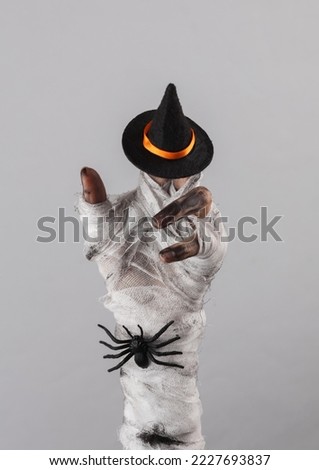 Mummy's hand wrapped in a bandage with witch hat and spider isolated on gray background. Halloween concept