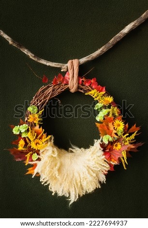 a wreath of vines in autumn yellow leaves hangs on a branch on an dark green background for a photo shoot of newborns