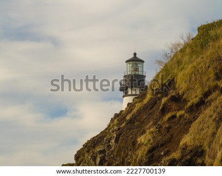 A lone white lighthouse on a high green ocean shore against a blue cloudy sky. Beautiful landscape. Postcard, banner. There are no people in the photo. There is free space to insert.