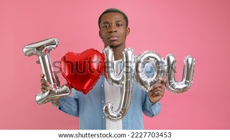 Seriously upset, unsmiling African-American in denim T-shirt demonstrates inscription I LOVE YOU standing on pink studio background. Parsing love, suffering without love.