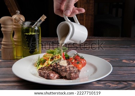 The chef's hand pours sauce over the steak. A piece of steak with salad and pepper sauce
