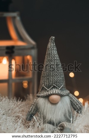 A cute dwarf, in a high hat, on skis and on a brown background, decorated with lanterns with a candle, cones and a garland. Suitable for postcards and Christmas greetings