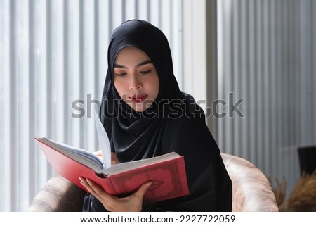The Quran. The Holy book of Muslims. Young Asian woman reading the Islamic Qur'an or Koran against the dark background to close to the teachings of Prophet or God. religion and faith concept