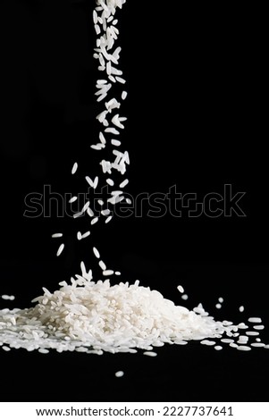 Raw white rice is falling on table. Pile of uncooked long rice on black background. Natural organic vegan food. Vertical photo.