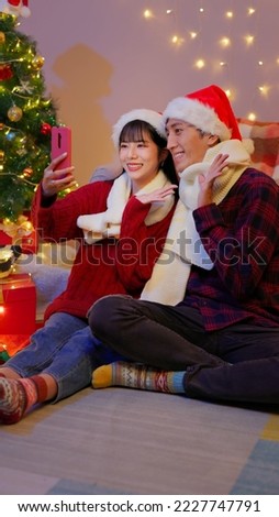 asian lovely young couple wearing christmas clothes are taking selfie with xmas tree at home