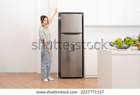 Asian woman standing next to the refrigerator in the kitchen Royalty-Free Stock Photo #2227771157