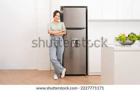 Asian woman standing next to the refrigerator in the kitchen Royalty-Free Stock Photo #2227771171