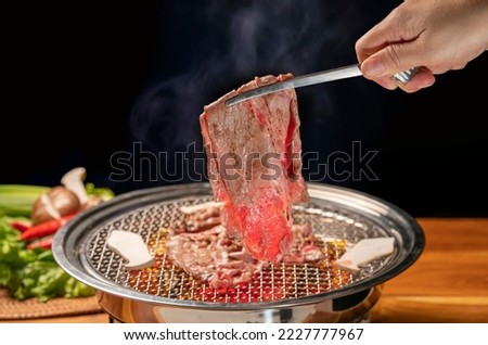 Hand using chopsticks to pick up wagyu beef on hot charcoal Asian BBQ food style, Grilled Beef Sirloin meat on the charcoal stove,Korean BBQ style. Royalty-Free Stock Photo #2227777967
