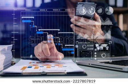 Businessman hand Project manager working and update tasks and Gantt chart scheduling virtual diagram.with smart phone, tablet and laptop in modern office. Royalty-Free Stock Photo #2227807819