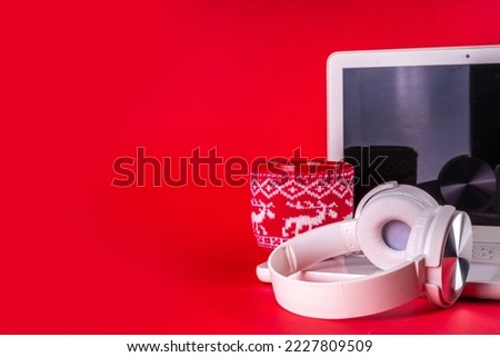 Festive red composition with white laptop computer, headphones, big cup for hot chocolate. Christmas mood and vibe, listen traditional new year songs music. Preparation for Christmas background