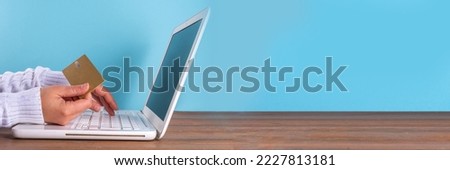 Woman hands doing online shopping, online payment with credit card simple background, white laptop with headphones, shopping cart, credit card wooden and light blue background copy space