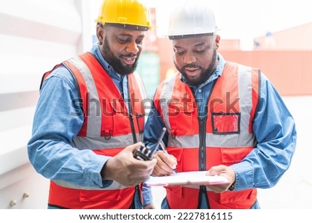Portrait photo of two black african male container engineers working and inspecting containers around a shipping yard of a local logistic freight  forwarder company Royalty-Free Stock Photo #2227816115