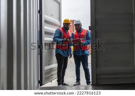 Portrait photo of two black african male container engineers working and inspecting containers around a shipping yard of a local logistic freight  forwarder company Royalty-Free Stock Photo #2227816123