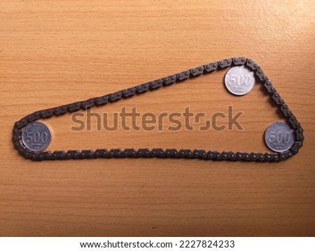 A gear chain with three Indonesian coins on the corners, illustrates the economic cycle. Shot at high angle.