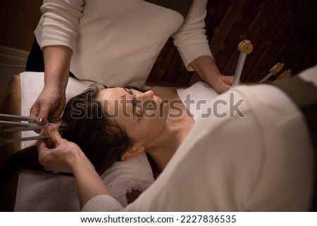 Couple of holistic doctors working with woman touching by resonating tuning forks to special points of body indoor. Sound therapy of alternative medicine Royalty-Free Stock Photo #2227836535