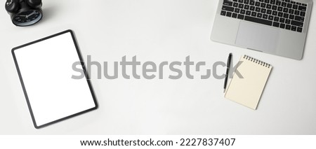 Top view of stylish desk with tablet empty screen and laptop computer, notebook and pen on white background
