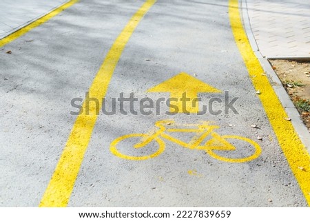 Outdoor bike path. Close-up of painted yellow bicycle sign and an arrow on pavement with stripes.