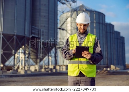A supplies worker uses a tablet in front of the silos. Royalty-Free Stock Photo #2227849733