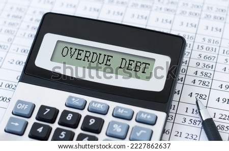 On the light table there is a black calculator with the text OVERDUE DEBT on the scoreboard, a pen and a white alarm clock. Business concept Royalty-Free Stock Photo #2227862637