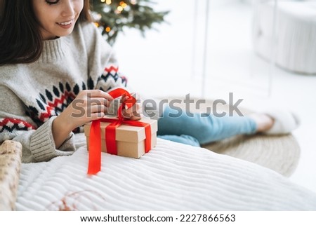 Crop photo of young woman in nordic sweater packing gift box at home