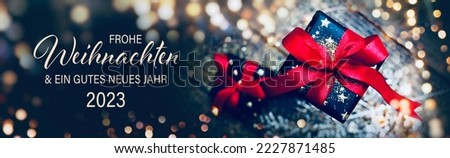 Christmas greeting card with text in German - Frohe Weihnachten means Merry Christmas and Happy New Year 2023 - Gift box with red bow and bokeh lights
