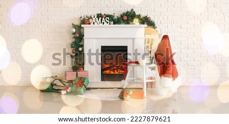 Fireplace with Christmas decor, gifts, chair and Santa Claus costume near white brick wall